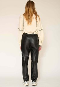 Blouse beige texturé avec des détails en noir associée à un pantalon en cuir noir. La tenue est complétée par des baskets argentées.