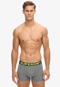 Graue Boxershorts mit einem schwarzen Bund, der gelben "SUPERDRY"-Aufschrift, enganliegendem Design, weicher Textur, geeignet für den Alltag.