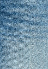 Ανοιχτό μπλε denim ύφασμα με ορατό διαγώνιο σχέδιο ύφανσης και μια κάθετη ραφή που διασχίζει το κέντρο.