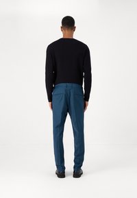 Un pull noir, un pantalon bleu à coupe ajustée et des chaussures noires. Le tissu semble lisse, avec un design épuré et sans motifs visibles.