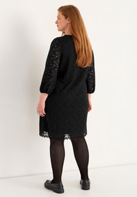 Svart spetsklänning med trekvartslånga ärmar, scallopad fåll, texturerad tyg och matchad med svarta strumpor och skor.