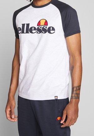Krótka koszulka z krótkim rękawem w jasnoszarym kolorze i granatowymi rękawami raglanowymi. Na froncie duże czarne logo „ellesse” z kolorowym symbolem słońca.