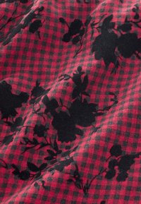 Material textil cu un model în carouri roșii și negre, cu siluete florale negre. Materialul pare moale și ușor texturat.