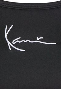 Melnas auduma topiņš ar izteiktu baltu izšūtu logotipu un paraksta stilu. Gluda tekstūra un pieguļoša forma ar minimālām šuvēm.