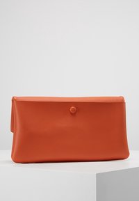 Oranžová kožená psaníčko s minimalistickým designem, s hladkým povrchem, zapínáním na knoflík a tvarem obálky.