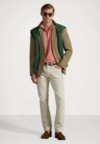 Μπεζ σακάκι houndstooth, ροζ πόλο, πράσινο πλεκτό πουλόβερ κρεμασμένο, ανοιχτόχρωμο παντελόνι, καφέ μονοκόμματα και μαύρα γυαλιά ηλίου. Απλός και κλασικός συνδυασμός.