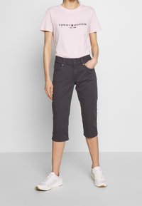 Světle růžové bavlněné tričko s logem "TOMMY HILFIGER", spárované s tmavě šedými kalhotami po kolena a bílými sportovními botami.