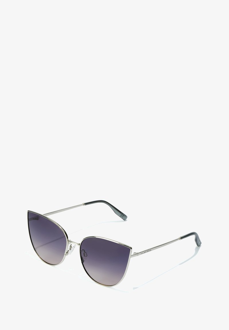 Ochelari de soare tip cat-eye cu lentile gri închis cu gradient, ramă metalică argintie și vârfuri negre pe brațe subțiri. Prezintă un design geometric.