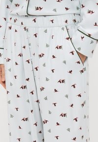 Lichtblauwe pyjama set met ingewikkelde patronen van rode vogels en groene bomen, met een elastische tailleband en knoopdetails op de broek.