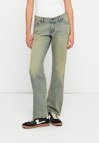 Calças de ganga verde-claras em corte reto, com passantes para cinto, cinco bolsos e um acabamento desbotado. Combinadas com ténis pretos.