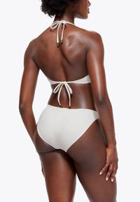 Bikini bianco con design a halter con lacci, tessuto morbido, slip a copertura media e eleganti dettagli metallici sui lacci.