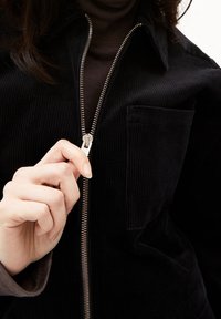 Czarna kurtka z weluru z zamkiem błyskawicznym i przednią kieszenią. Tkanina ma prążkowaną fakturę i kołnierzyk.