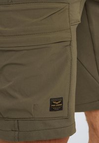 Shorts cargo kaki avec de multiples poches, une étiquette affichant "PME Legend", et un tissu texturé. Les coutures sont visibles le long des bords.