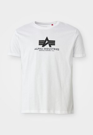 Fehér pamut póló, fekete grafikával ellátott logóval, amelyen egy "A" és két vízszintes csík található, felirattal: "Alpha Industries" és alatta a helyszín részleteivel.