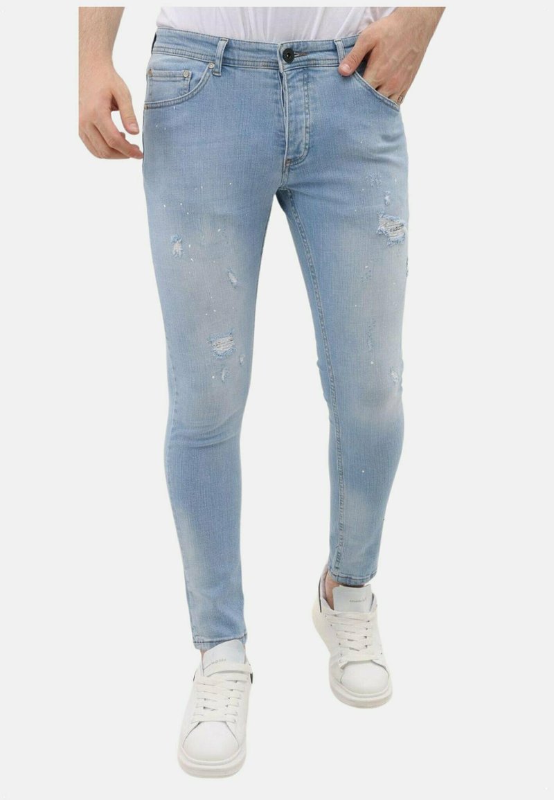 Lichtblauwe skinny jeans met versleten details, waaronder scheuren en vervaging. Draagt met witte sneakers. Heeft een klassiek vijf-pocket ontwerp.