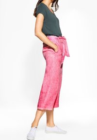 Růžové lněné culottes s opaskem na zavázání, se bočními kapsami. V kombinaci s krátkým šedým topem a bílými teniskami.