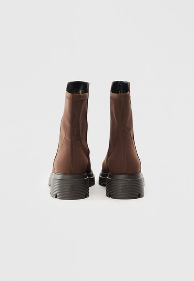 Brūni potītes zābaki ar gludu tekstila augšdaļu, melnu iekšpusi un ribotu gumijas zoli. Izceļas ar elegantu dizainu un minimālu šuvju skaitu.