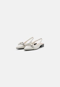 Des chaussures slingback blanches en cuir avec un bout pointu, ornées d'une chaîne métallique sur le dessus et d'un petit talon noir en bloc.