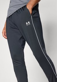 Melni sporta bikses ar baltām sānu svītrām un Under Armour logo. Iezīmes: elastīga josta, gluda auduma, un kabatas sānos.