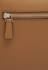 Superficie de cuero marrón con un acabado texturizado que presenta un cierre de cremallera dorado y un pequeño tirador de cremallera de cuero.