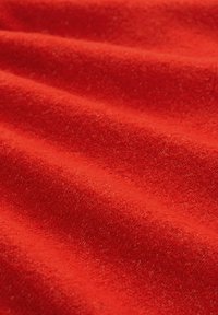 Czerwony materiał o miękkiej, teksturowanej powierzchni, z widocznym splotem i fałdami. Kolor jest intensywny i jednolity na całej powierzchni tkaniny.