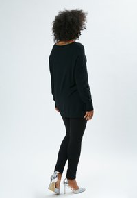 Maglione nero oversize con maniche lunghe, abbinato a leggings neri e tacchi alti argentati. Il maglione presenta un collo rotondo e una texture morbida.