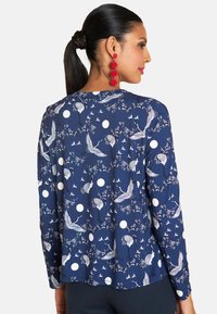 Marineblaues Langarmblusenshirt mit einem weißen Kranich- und Blumenmuster, akzentuiert mit runden weißen Punkten. Weicher Stoff mit entspannter Passform.