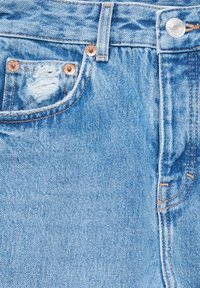 Jeans in denim leggermente blu con effetto usurato, dotati di tasca frontale, hardware in rame e dettagli di cucitura visibili. Tessuto morbido e textured.