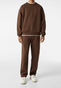 Survêtement marron en tissu doux. Sweat à col ras du cou avec des manches longues et des poignets côtelés, associé à un pantalon droit et des baskets blanches.
