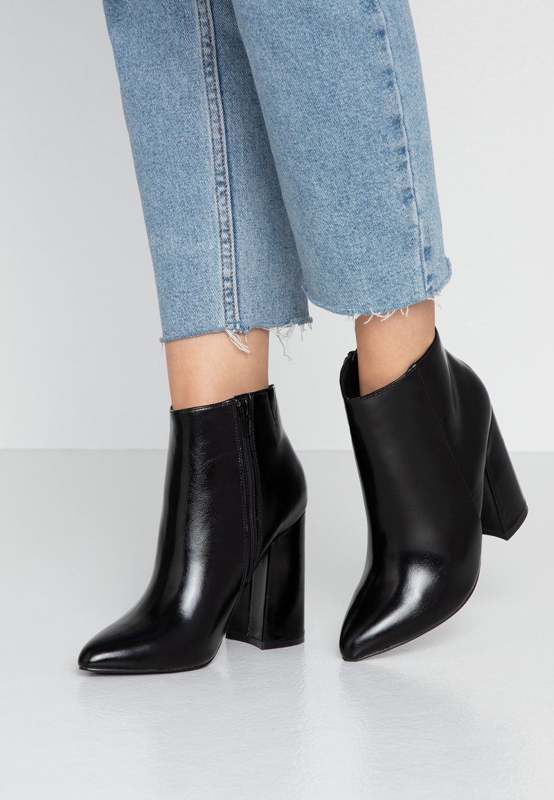 Bottes courtes en cuir noir à bout pointu avec talons blocs portées avec un jean denim bleu clair coupé au-dessus de la cheville avec des ourlets effilochés.
