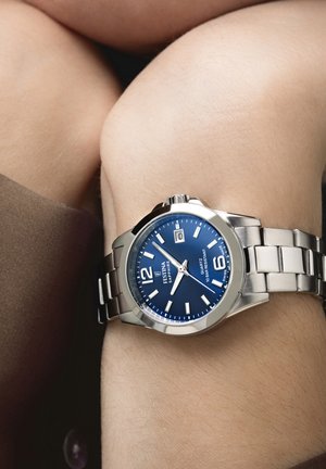 Orologio da polso in acciaio inossidabile argento con quadrante blu, indicatori delle ore bianchi, display della data e un comodo bracciale a maglie in metallo.