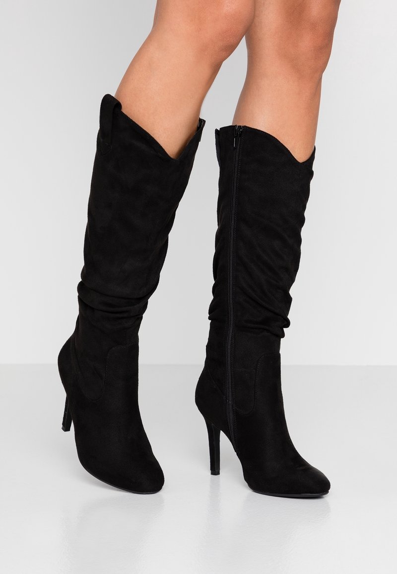 Botas negras hasta la rodilla, hechas de suave ante, con punta afilada, tacón alto de aguja y cierre de cremallera lateral.