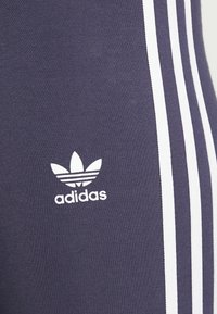 Navy urheiluhousut valkoisilla sivuviivoilla ja suurella valkoisella Adidas-logolla. Sujuva pinta, istuva muotoilu ja joustava kangas.