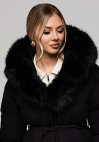 Černá péřová bunda s velkým umělým kožešinovým límcem, s krémovým vnitřním podšíváním, předním zipem a páskem v pase. Měkká textura.