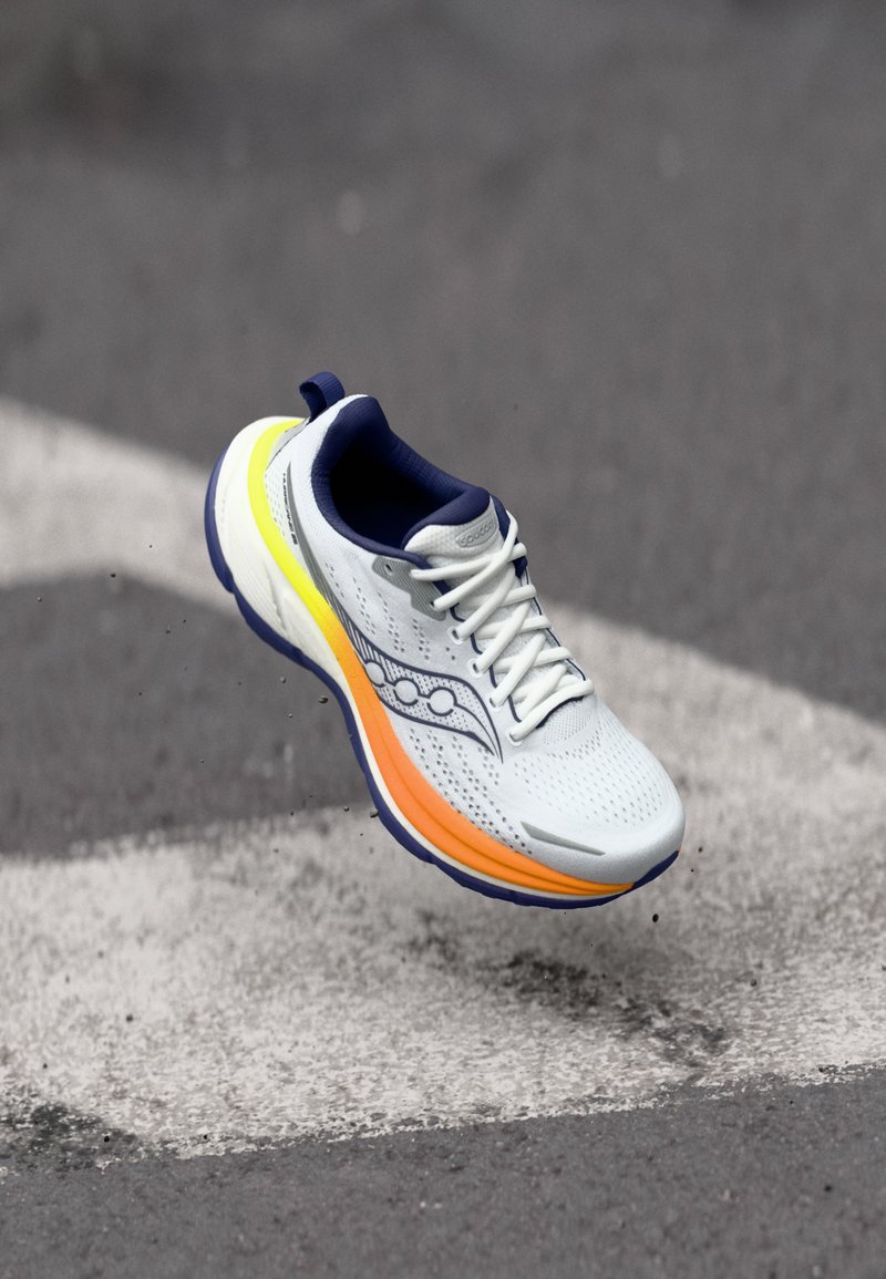 Valge sportjalats tekstureeritud ülemise osaga, millel on tumesinised aktsendid ja erksate kollase-oranži tooni gradiente tald. Paeltega kinnitamine koos logo detailiga.