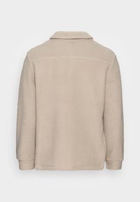 Beige fleece jacket with a textured surface, long sleeves, a folded collar, and a straight hem. No visible closure or embellishments.