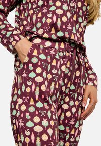 Daugiakspalvis pižamos komplektas su bordo pagrindu ir linksmu šventiniu raštu, kuriame vaizduojami žaisliukai, riešutų griebikliai ir gulbės. Komplekte yra kišenės.