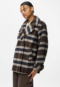 Cappotto doppiopetto a righe marroni e blu navy con colletto a scollo, tasche laterali e materiale in pile testurizzato. Bottoni neri accentuano il design.