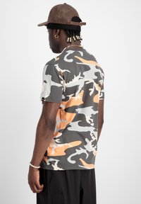 T-shirt med kort ärm i camouflage, i grått, orange och vitt. Mjuk tyg med avslappnad passform. Bakifrån visas ett abstrakt mönster och ljusa sömmar.