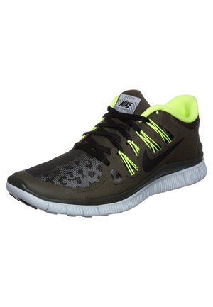 Chaussure de course Nike vert foncé et noir avec lacets et doublure jaune néon, semelle blanche flexible et zone des orteils à motif.