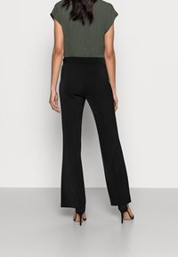 Svarta utsvängda byxor med en slät textur, hög midja och sömdetaljer, kombinerat med en olivgrön kortärmad topp.