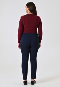 Maglione bordeaux a maglia con dettaglio sulle spalle scoperte, abbinato a pantaloni blu scuro aderenti e scarpe basse nere. Tessuto morbido e vestibilità aderente.