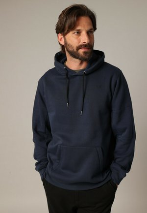 Sweatshirt bleu marine avec cordons de serrage, poche frontale et texture douce. Présente un logo subtil, une coupe décontractée et des poignets côtelés.