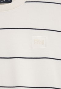 Pull blanc avec de fines rayures horizontales noires et un petit écusson blanc sur la poitrine indiquant "POLO CLUB".