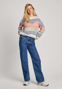 Pleteni pulover u krem, plavoj, koraljnoj i sivoj boji s valovitim prugama; nosi se s svijetloplavim širim trapericama i bijelim tenisicama.