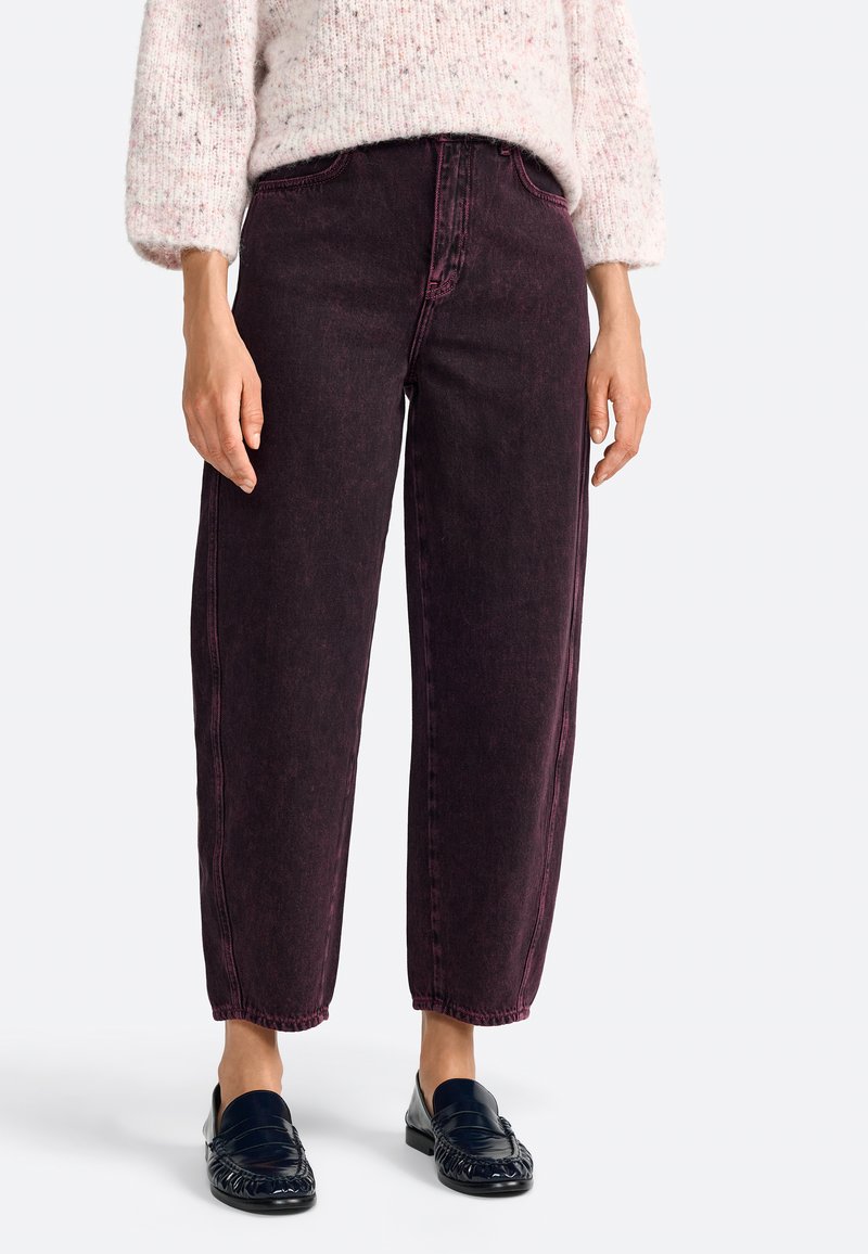 Jeans a vita alta di un borgogna scuro con taglio dritto, caratterizzati da cuciture visibili e una texture leggermente sbiadita. Abbinati a mocassini neri.