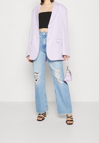 Fialový oversize blazer, černý crop top, vysoce pasové roztrhané modré džíny a černé sandály s pásky, doplněné o malou fialovou kabelku.