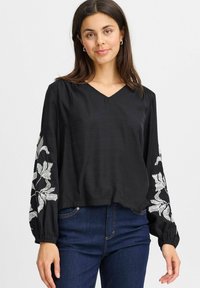 Blusa nera con scollatura a V e maniche lunghe, caratterizzata da ricami floreali bianchi sulle maniche. Tessuto leggero con una vestibilità comoda.