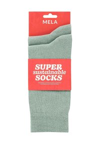 Chaussettes en coton vert affichées sur une carte rouge avec du texte, mettant en avant la durabilité. Texture lisse, bord supérieur côtelé, certification commerce équitable.