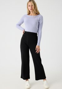 Suéter de punto lila claro con detalles acanalados y mangas largas, combinado con pantalones de pierna ancha negros de cintura alta y zapatillas blancas.